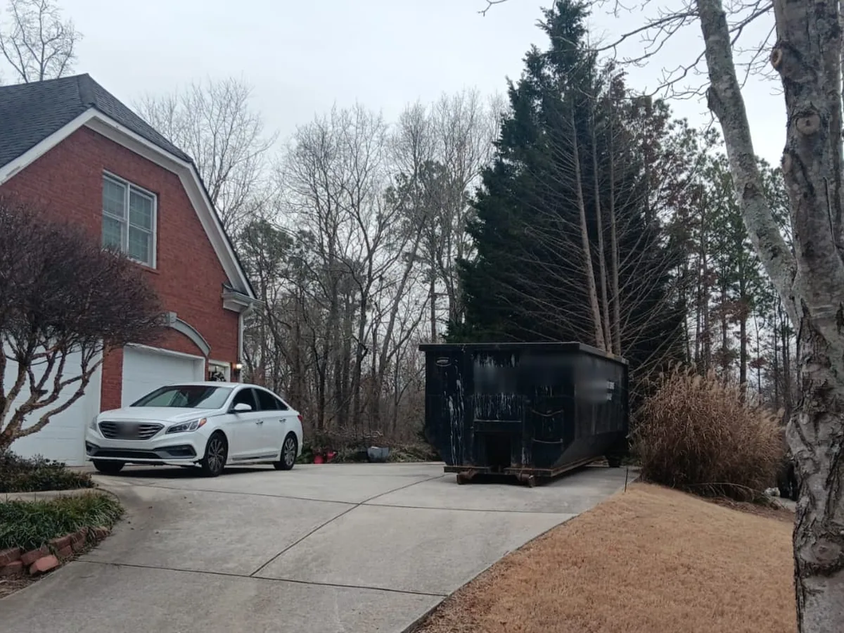 Black roll-off dumpster in a driveway beside a brick house and garage, 30 yard dumpster rental