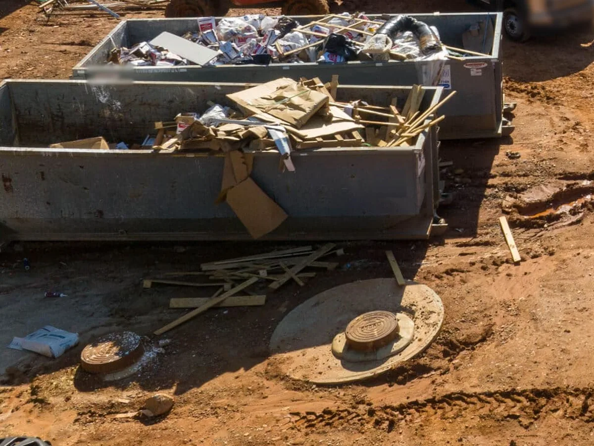 Roll-off dumpsters loaded with framing lumber, cardboard and packaging on a red clay jobsite, 40 yard dumpster rental