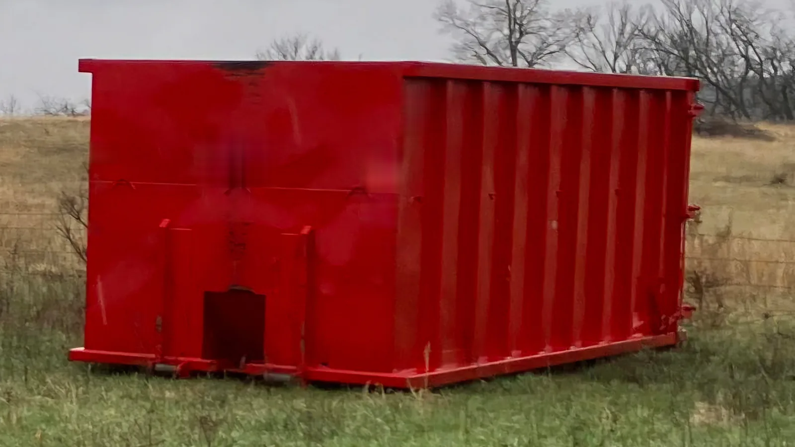 Tall red roll-off dumpster with high steel walls on a dry grass lot, 40 yard dumpster rental