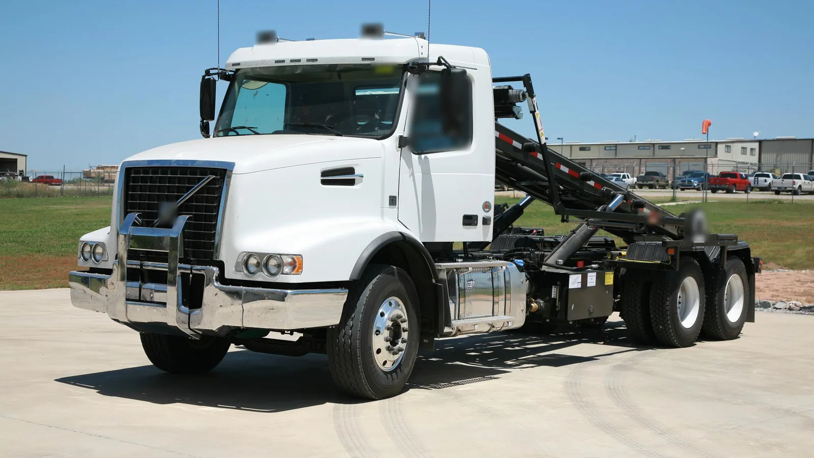 White roll-off truck parked on a concrete lot beside a mowed field, roll-off dumpster rental
