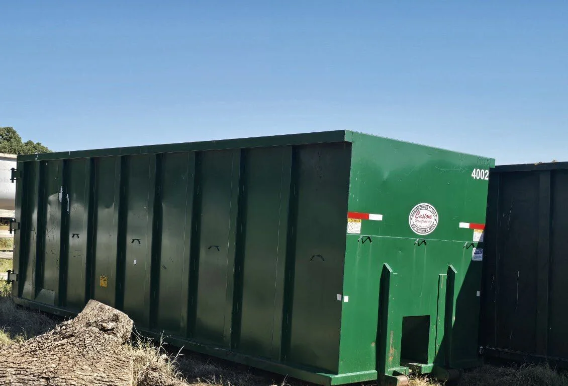 Green roll-off dumpster beside a black roll-off dumpster on a lot, commercial dumpster rental