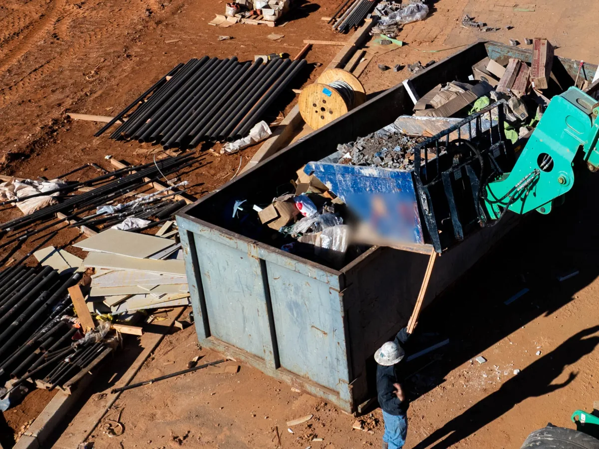 Telehandler dumping construction debris into a roll-off dumpster on a red clay jobsite, construction dumpster rental