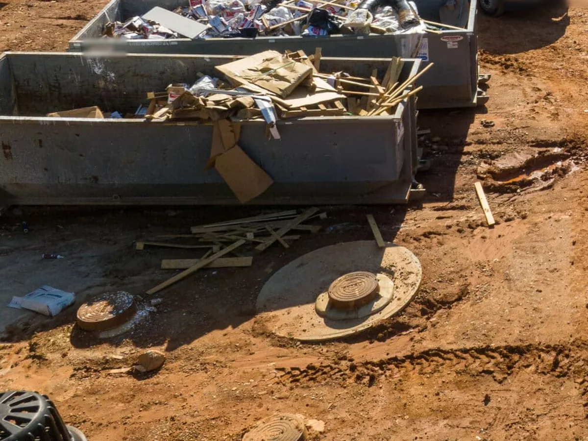 Roll-off dumpsters holding framing lumber, cardboard and packaging at a red clay jobsite, construction dumpster rental