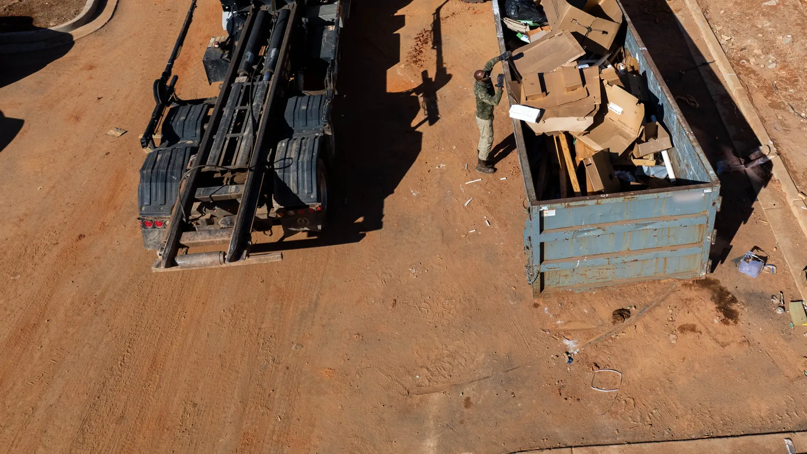 Aerial view of a roll-off truck beside a roll-off dumpster filled with cardboard on a construction site, construction dumpster rental