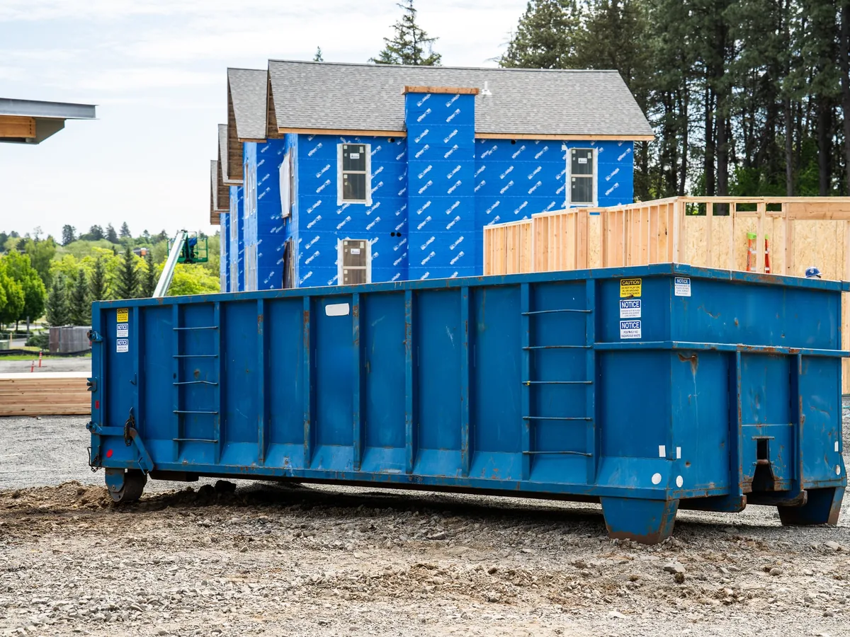 Tall blue roll-off dumpster at an apartment construction site with framed walls behind it, construction dumpster rental