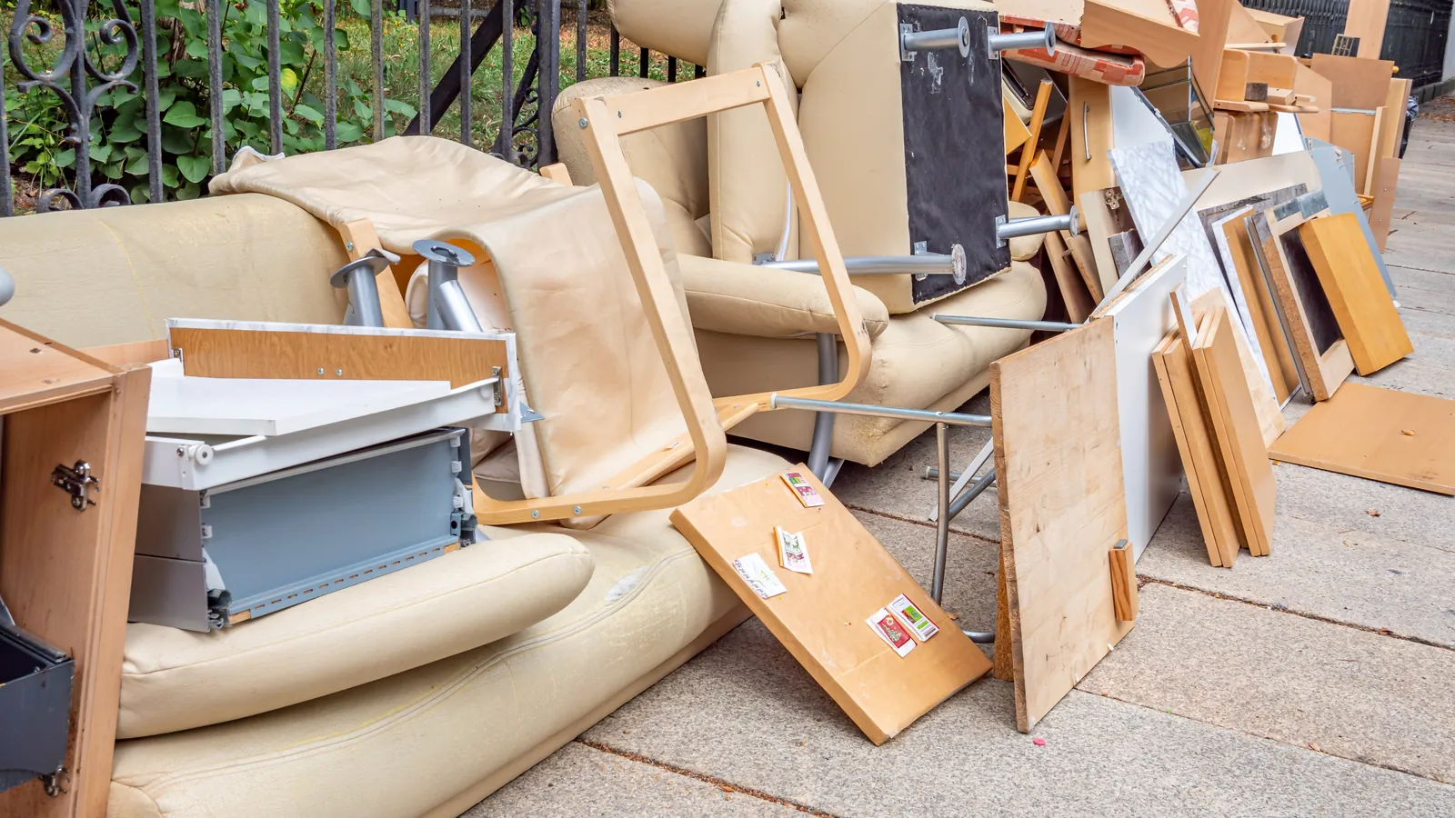 Old couch, chairs and particle board furniture piled on a sidewalk for removal, dumpster rental vs junk removal