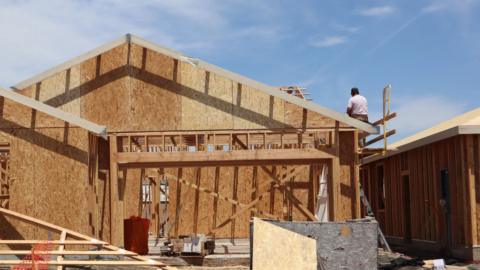 Wood-framed house under construction with stacked lumber on the lot, roll-off dumpster rental