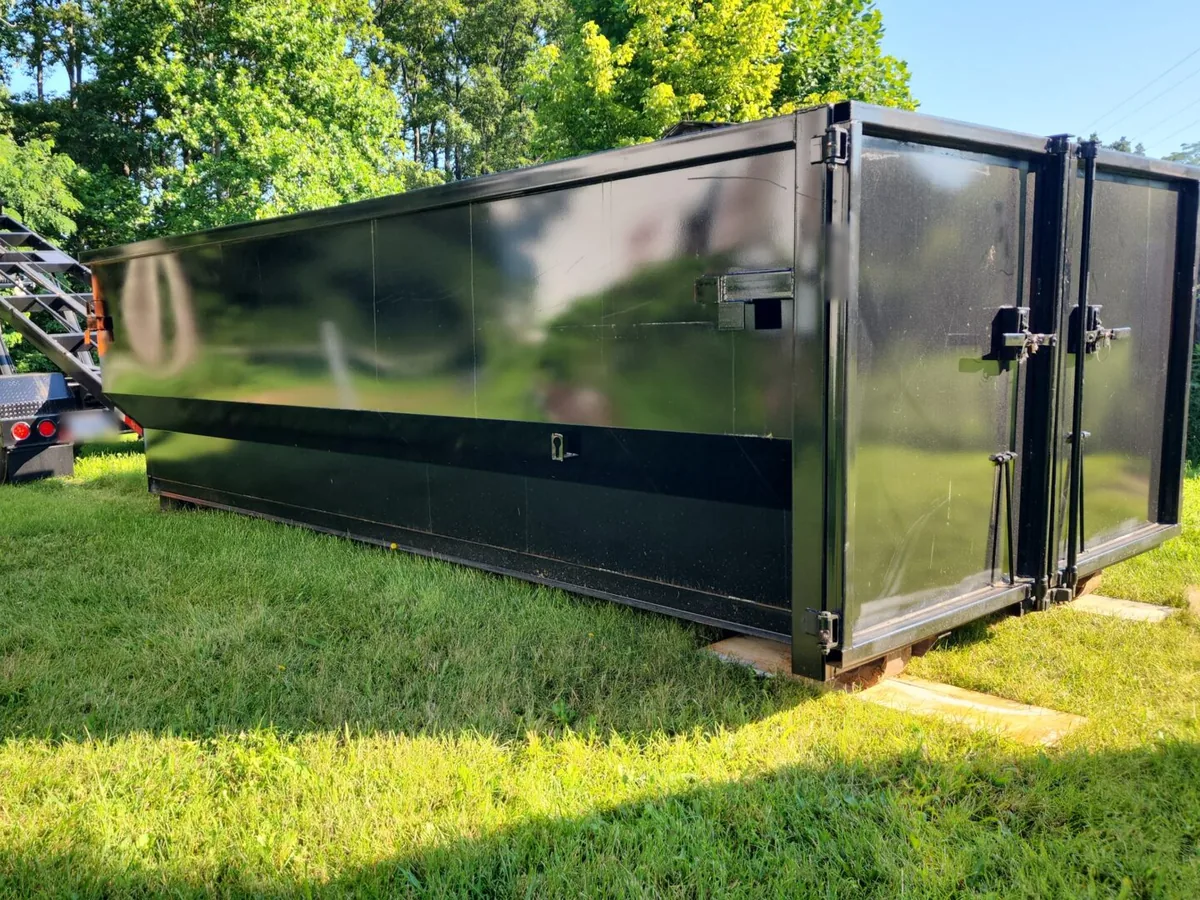 Black roll-off dumpster set on wood boards on a grassy yard, residential dumpster rental