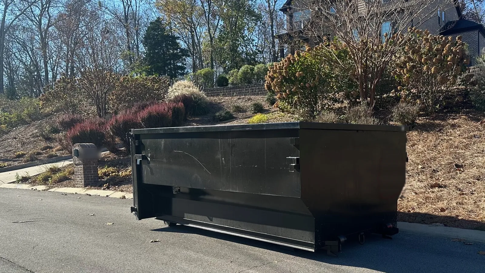 Black roll-off dumpster at the curb of a landscaped residential street, residential dumpster rental