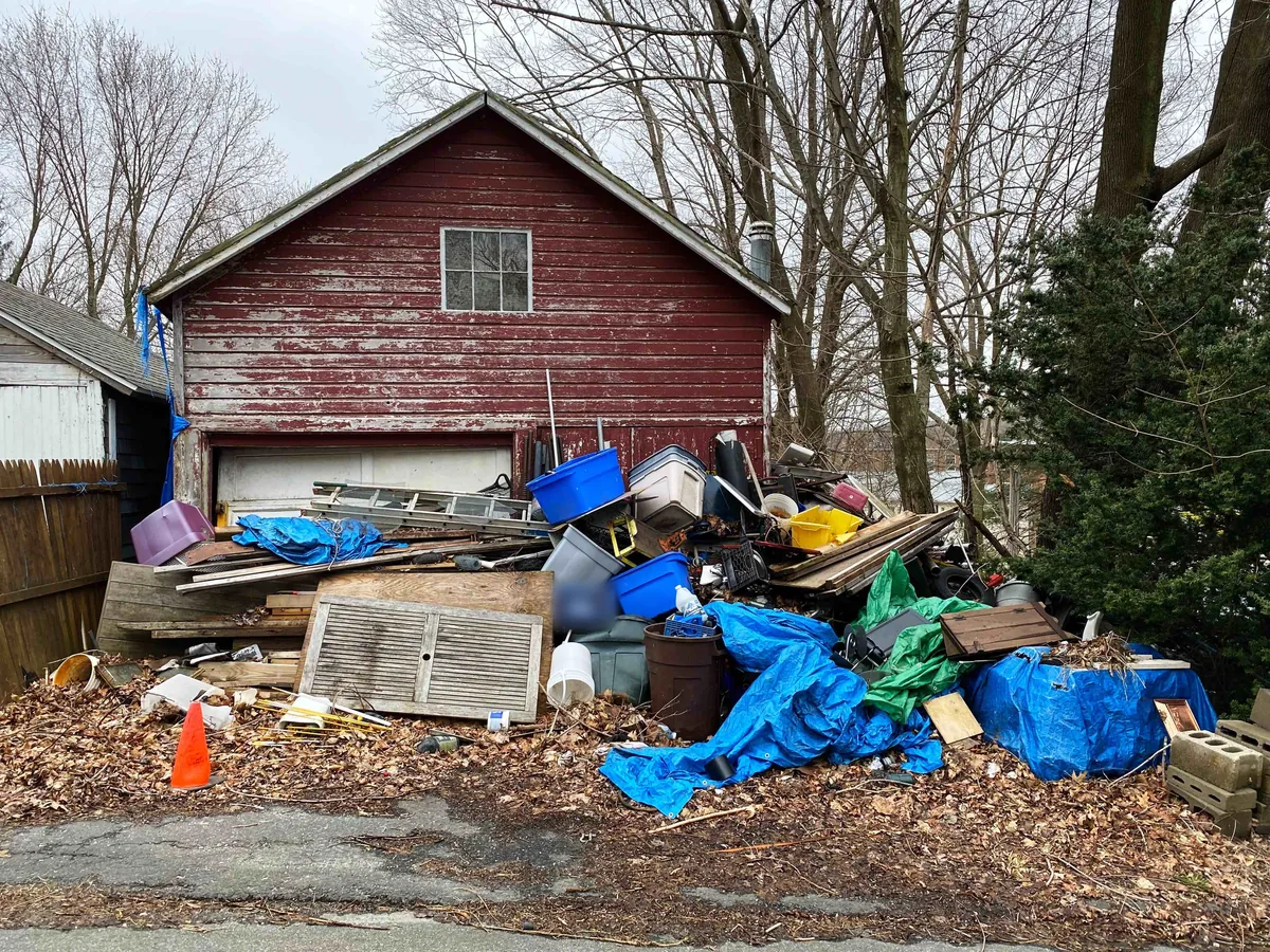 Garage cleanout pile of bins, lumber, tarps and old furniture beside a red garage, residential dumpster rental