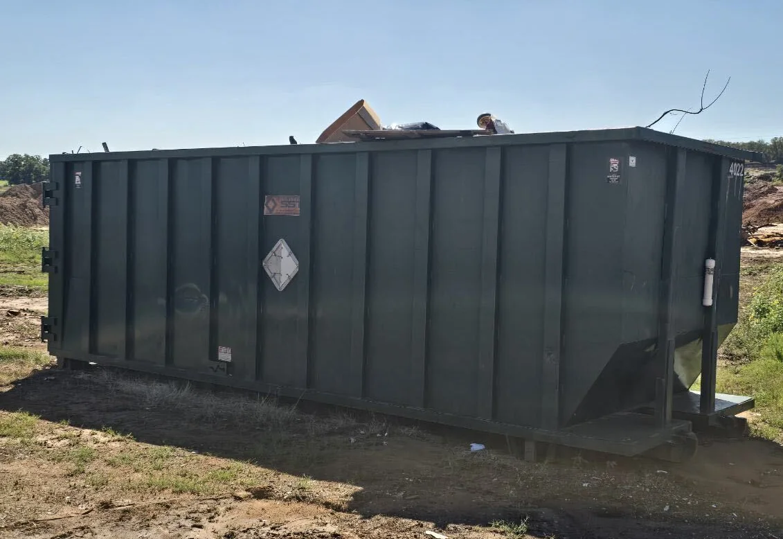 Dark green roll-off dumpster loaded to the top on a dirt lot, same-day dumpster rental