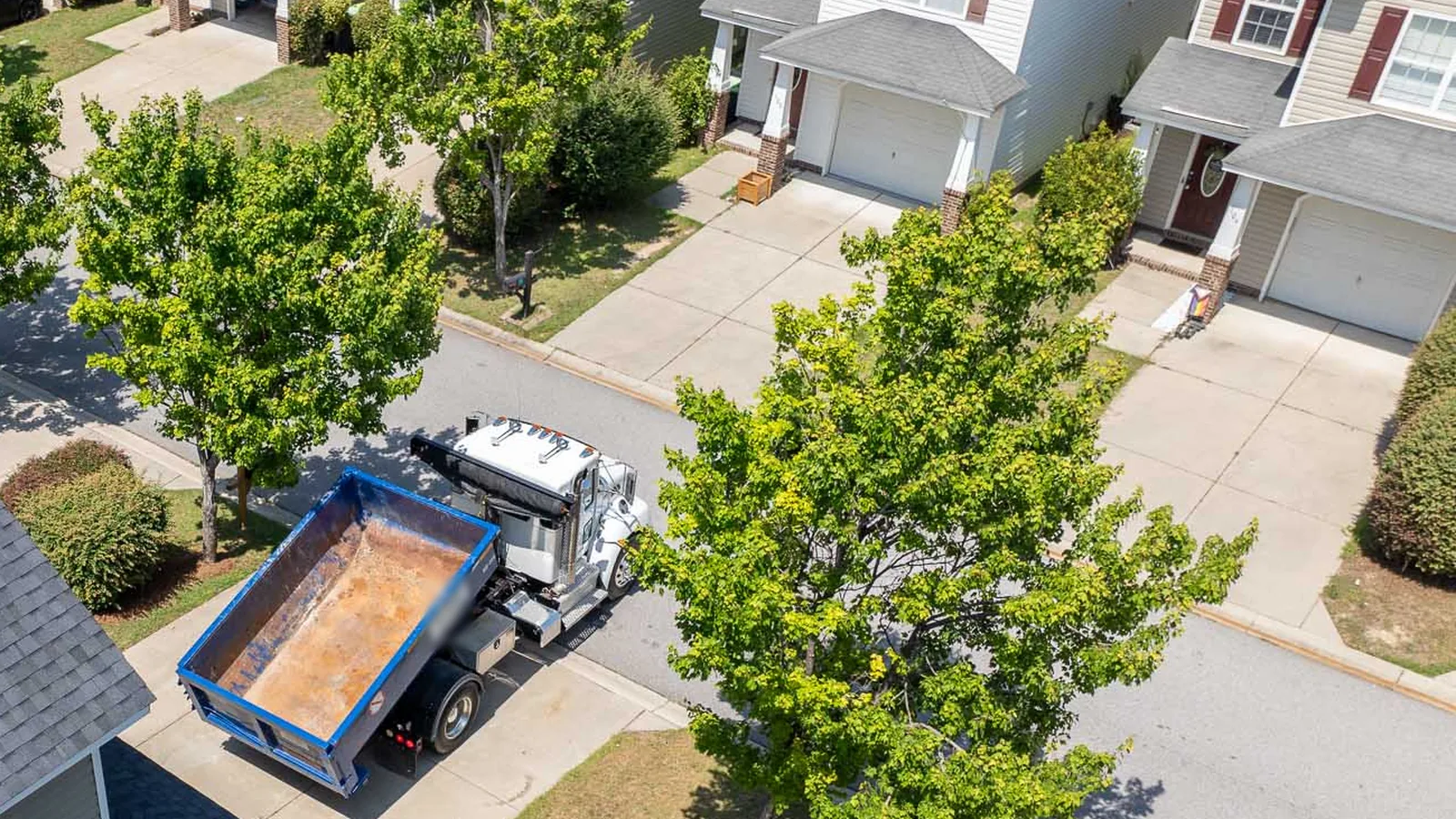 Roll-off truck setting an empty blue roll-off dumpster in a suburban driveway, roll-off dumpster rental